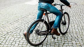 A person riding a VanMoof Electrified S bicycle on a cobblestone street.
