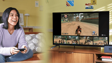 Eine Frau spielt Nintendo Switch, während ein Fernseher ein Rennspiel und vier Spieler-Video-Feeds zeigt.