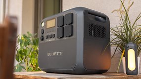 A Bluetti AC200L portable power station on a wooden table with a plant and a lantern nearby.