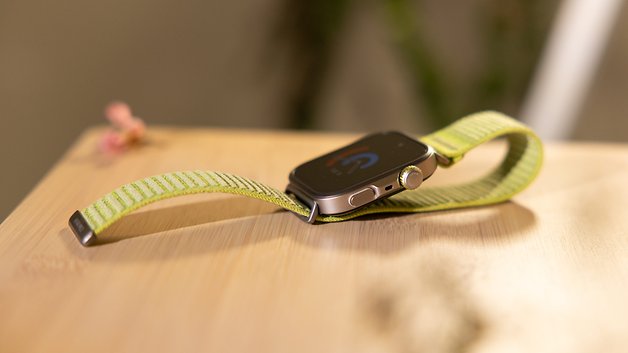 Eine Huawei Watch Fit 4 Pro auf einer Holzoberfläche mit einem grün gestreiften Armband.