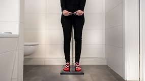 Personne debout sur une balance dans une salle de bain, tenant un outil de mesure.