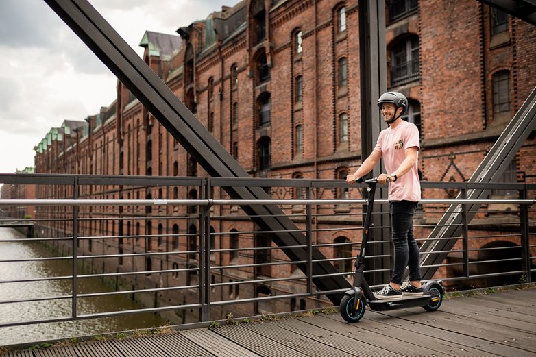Achtet darauf, E-trottinette wie den Ninebot MAX G30D II mit Helm zu fahren. Mann fährt den E-trottinette auf einer Brücke