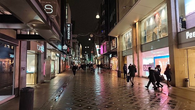 A busy shopping street at night, with illuminated shop windows and passers-by.