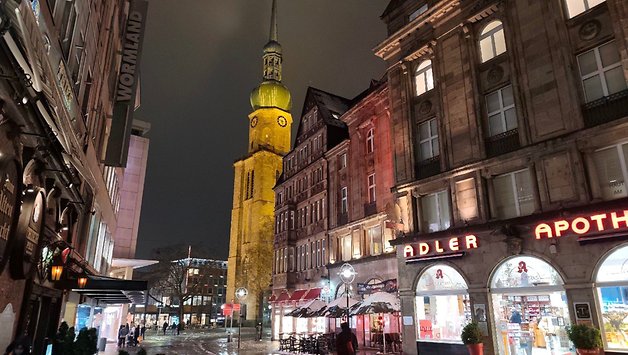 A rainy night view of a street with historic buildings and a clock tower.