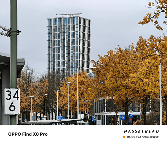 Bâtiment moderne avec façade en verre parmi des arbres d'automne, pris avec OPPO Find X8 Pro.