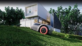 Ein Mähroboter auf einem grasbewachsenen Hang neben einem modernen Haus.