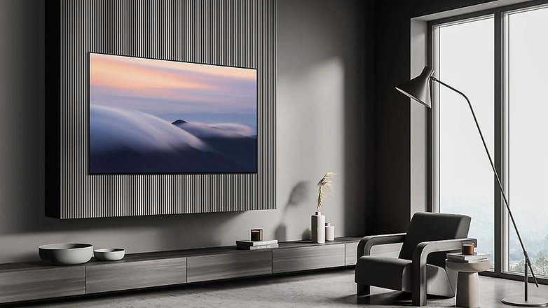 Ein schlanker Samsung S90D Fernseher, der an einer strukturierten Wand in einem modernen Wohnzimmer montiert ist, mit einem stilvollen Sessel. Ein schlanker Samsung S90D Fernseher, der an einer strukturierten Wand in einem modernen Wohnzimmer montiert ist, mit einem stilvollen Sessel.