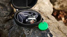 A black zippered case on a rock containing a headlamp and a green Chipolo-Pop tracking tag.