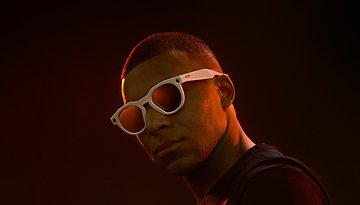 A person wearing white sunglasses against a dark background.