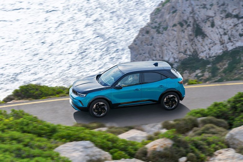 Une Opel Mokka Electric (2025) bleue et noire roulant le long d'une route côtière au bord de la mer. Une Opel Mokka Electric (2025) bleue et noire roulant le long d'une route côtière au bord de la mer.
